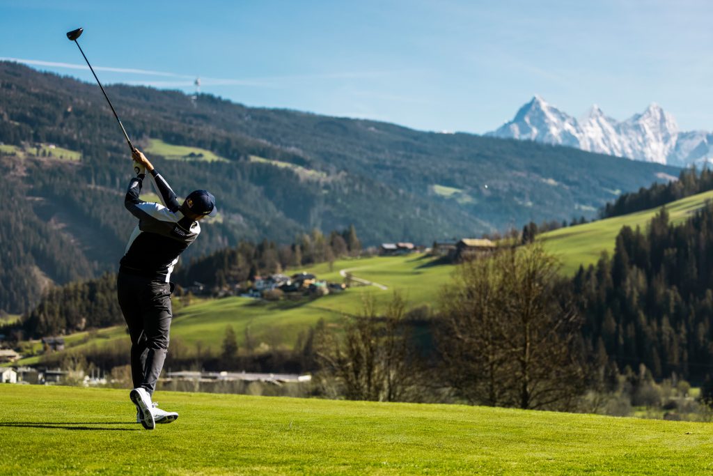 Sunny hotel terrace with sun loungers, view of golf course and mountains during summer vacation in Radstadt